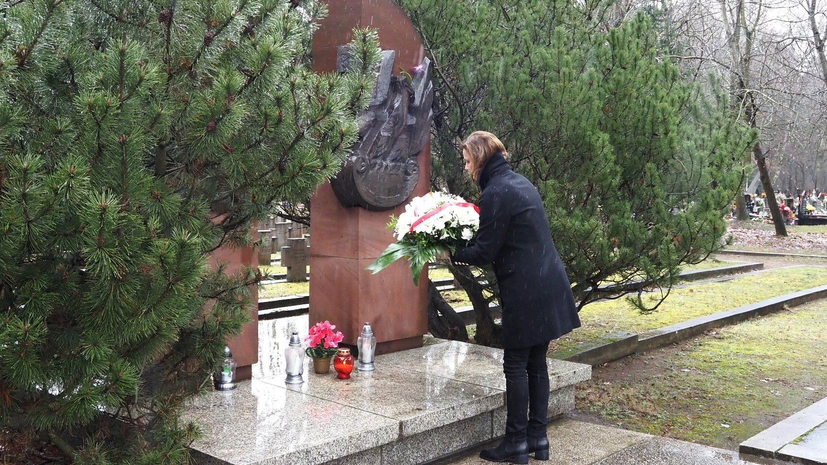 Zdjęcie przedstawia kobietę skłądajacą kwiaty pod pomnikiem.