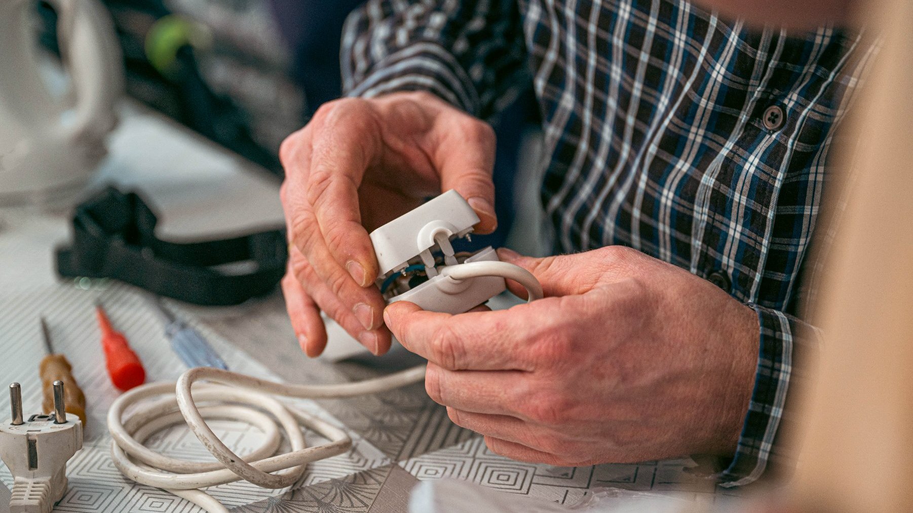 Na zdjęciu dłonie seniora naprawiającego wtyczkę kabla