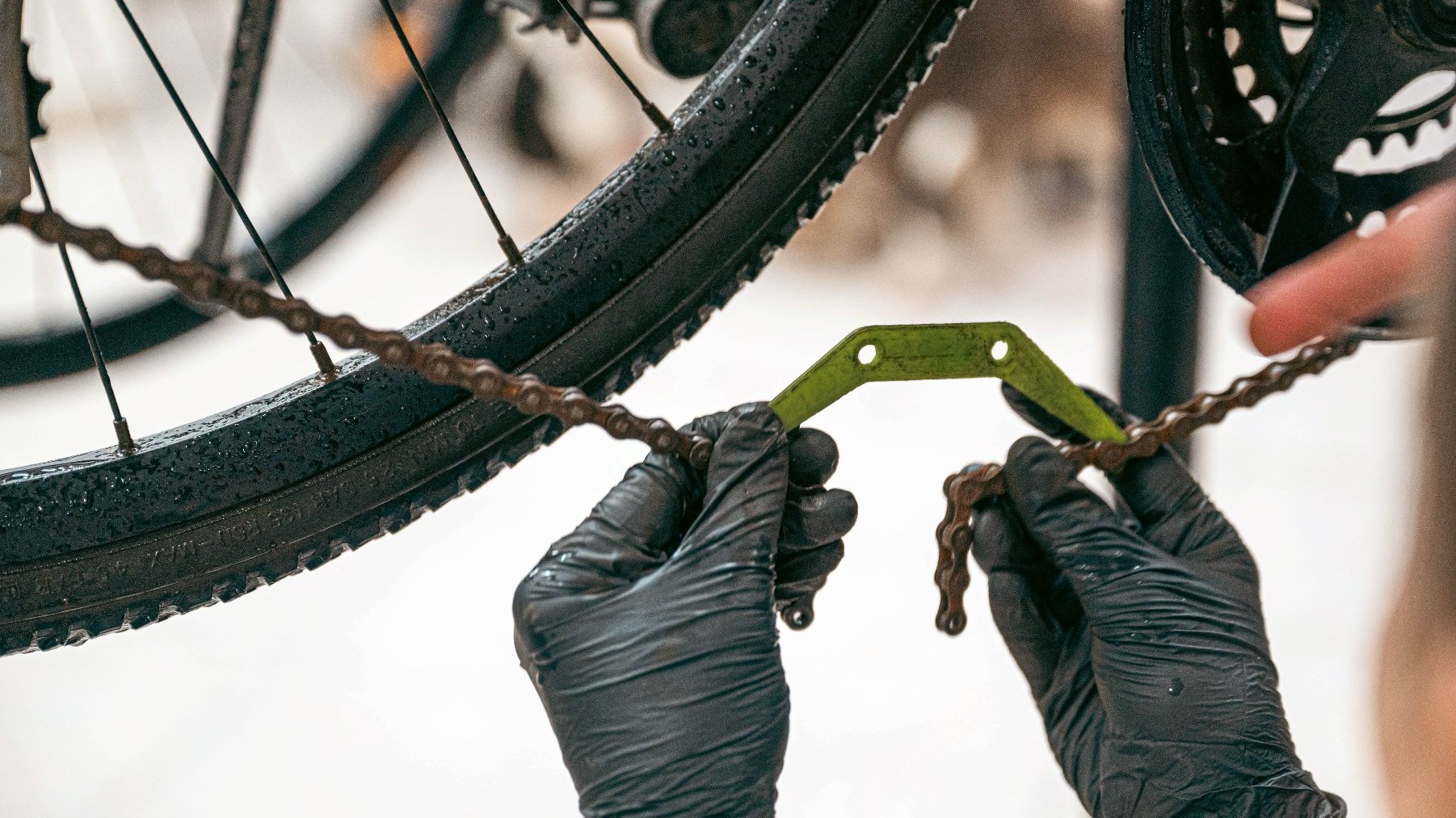 Na zdjęciu dwie dłonie w ciemnych rękawiczkach naprawiające łańcuch roweru