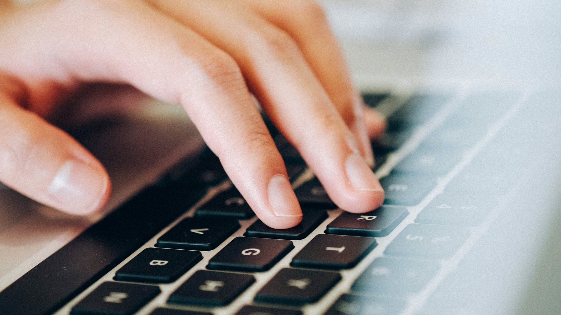 Zdjęcie przedstawia rękę piszącą na klawiaturze laptopa.