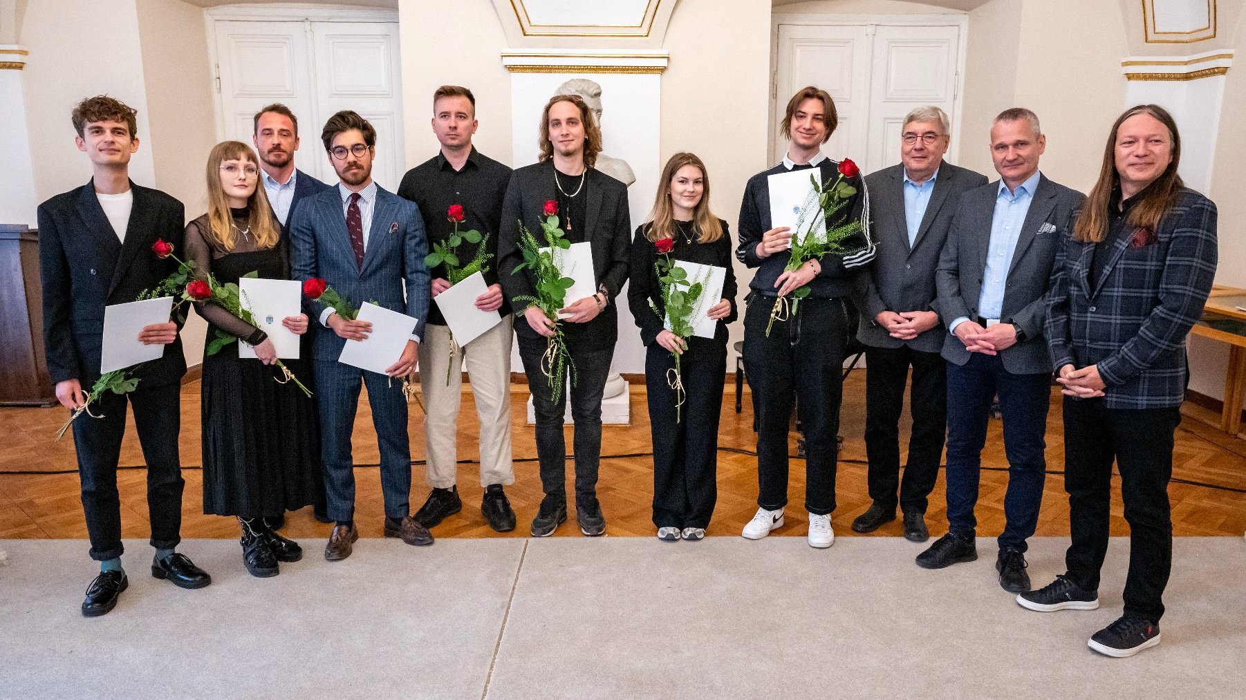 Zdjęcie przedstawia grupę osób pozujących do zdjęcia, Niektóre trzymają w dłoniach dyplomy i róże. - grafika artykułu