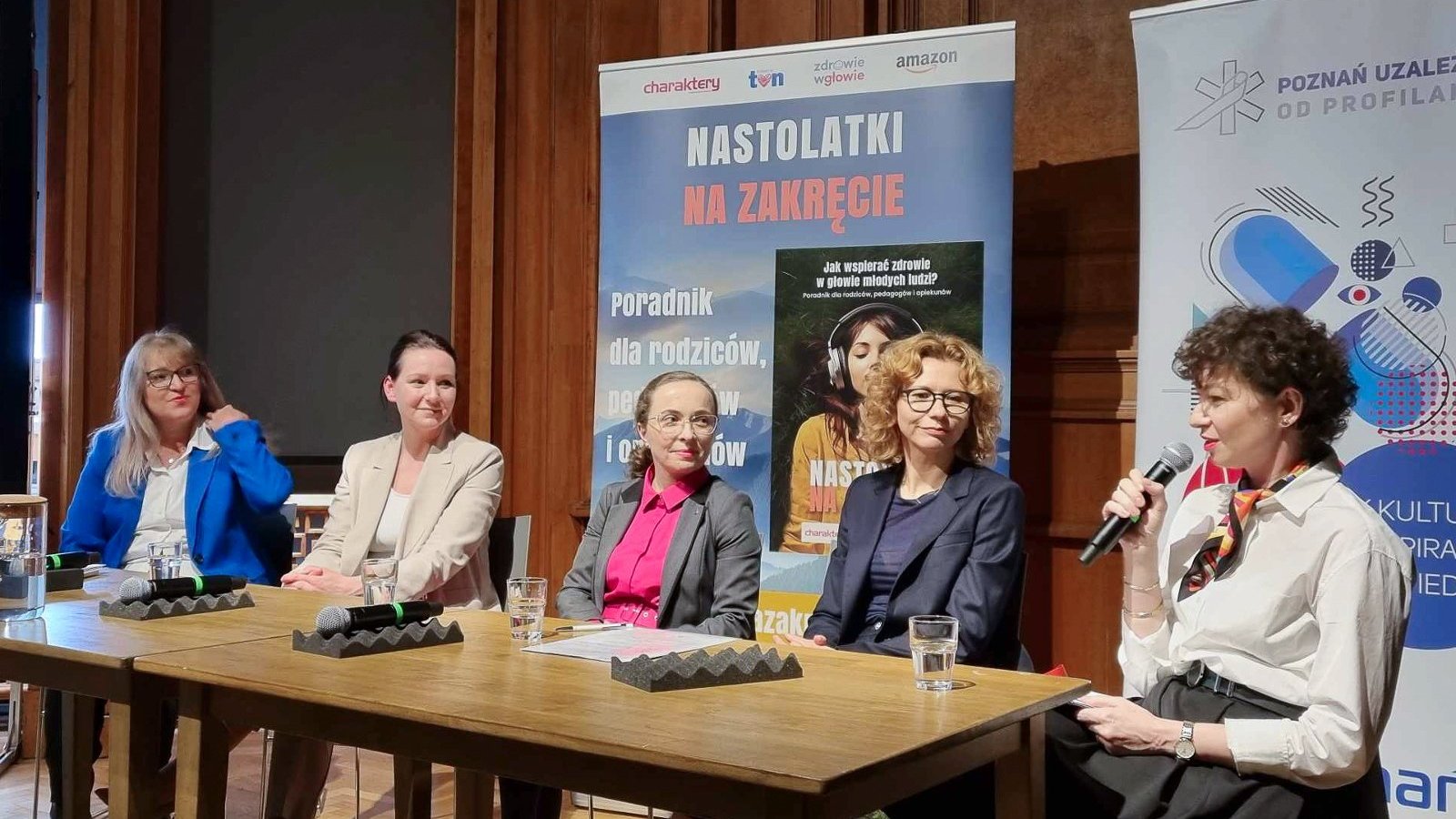 Na zdjęciu pięć kobiet za stołem, jedna z nich trzyma mikrofon