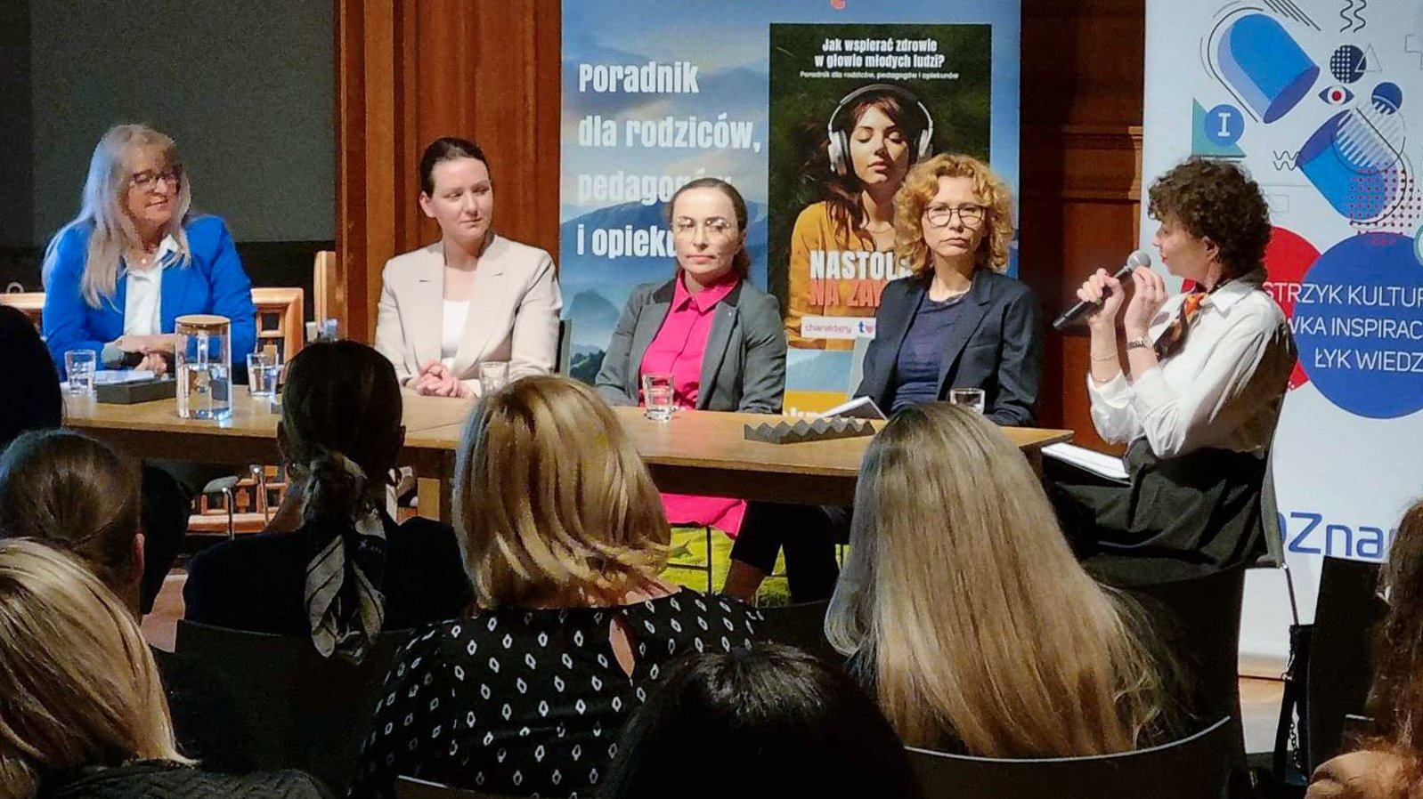 Na zdjęciu pięć kobiet za stołem, na pierwszym planie słuchająca ich publiczność