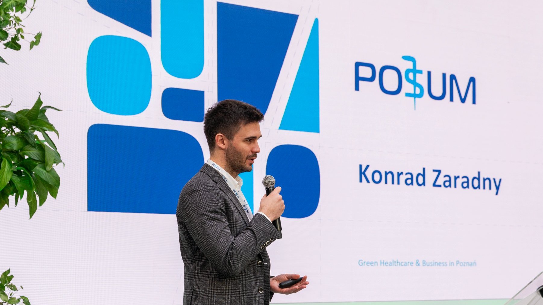 Na zdjęciu meżczyzna z mikrofonem w ręku, stoi profilem do obiektywu, w tle logo POSUM