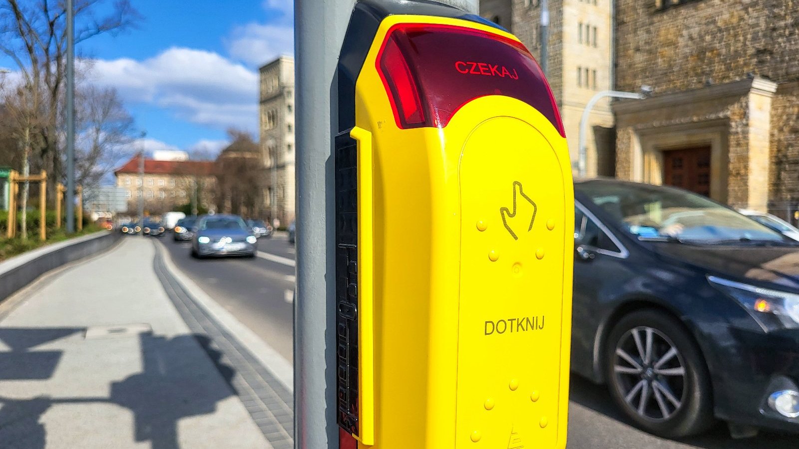 Zdjęcie przedstawia żółty przycisk na słupie sygnalizacji świetlnej.