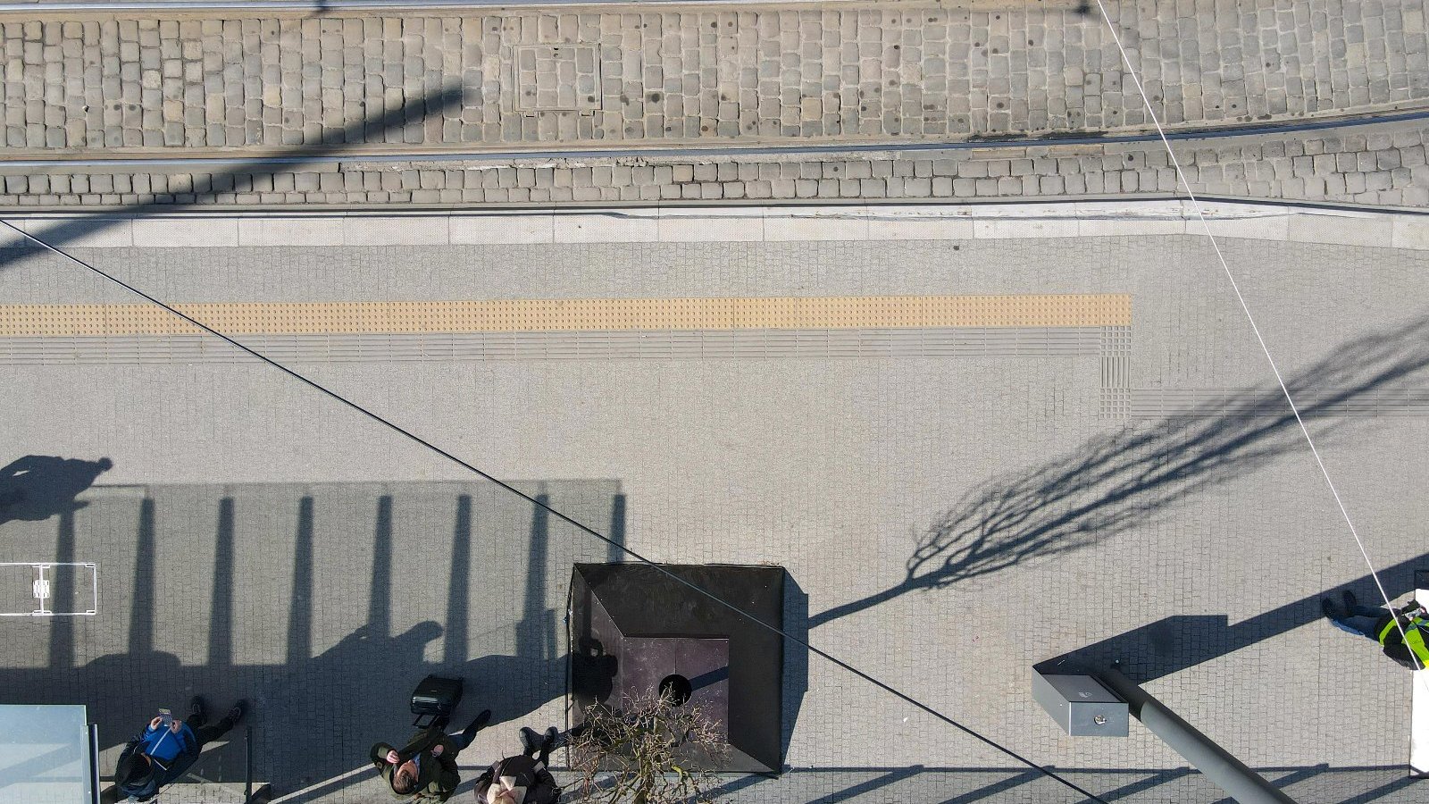 Zdjęcie przedstawia przystanek z lotu ptaka. Widać m.in. tory tramwajowe i pas żółtej nawierzchni fakturowej.