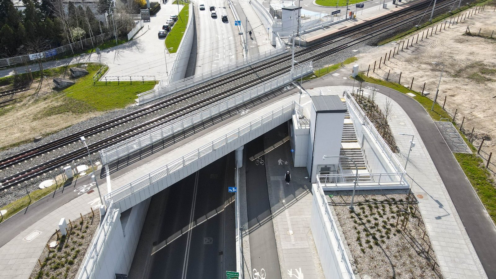 Zdjęcie przedstawia wiadukt kolejowy na jezdnią, drogą rowerową i chodnikiem. Na fotografii widać także windę.