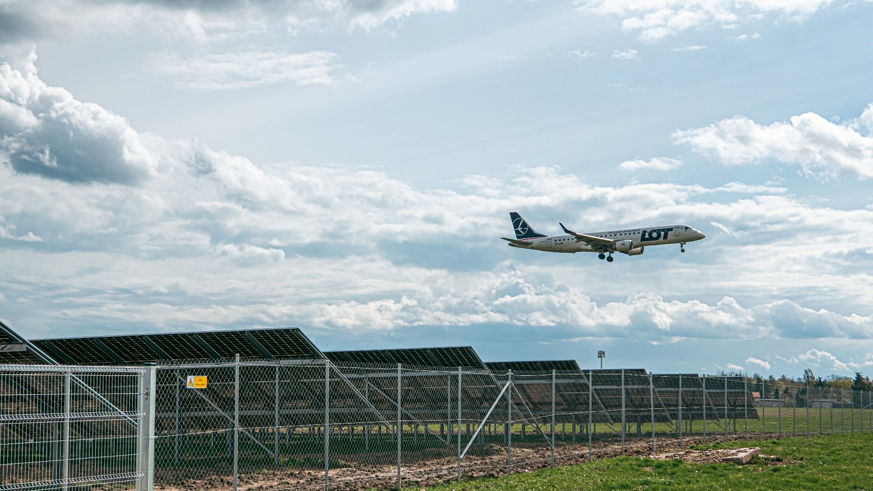 Na zdjęciu panele wotowoltaiczne, nad nimi leci samolot