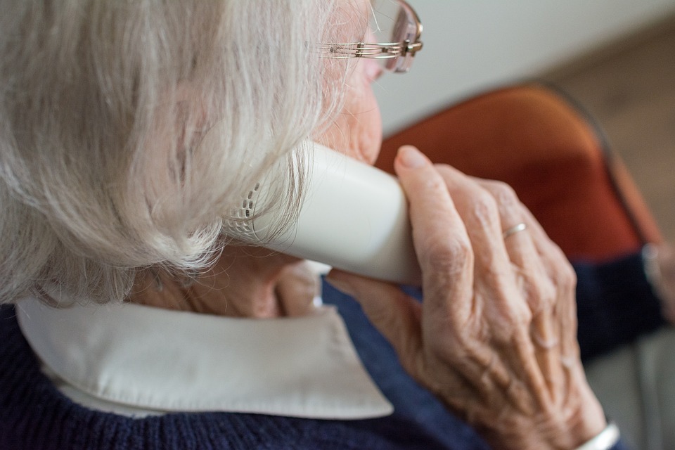 Na zdjęciu kobieta trzymająca słuchawkę telefonu przy uchu, siedząca tyłem do obiektywu - grafika artykułu