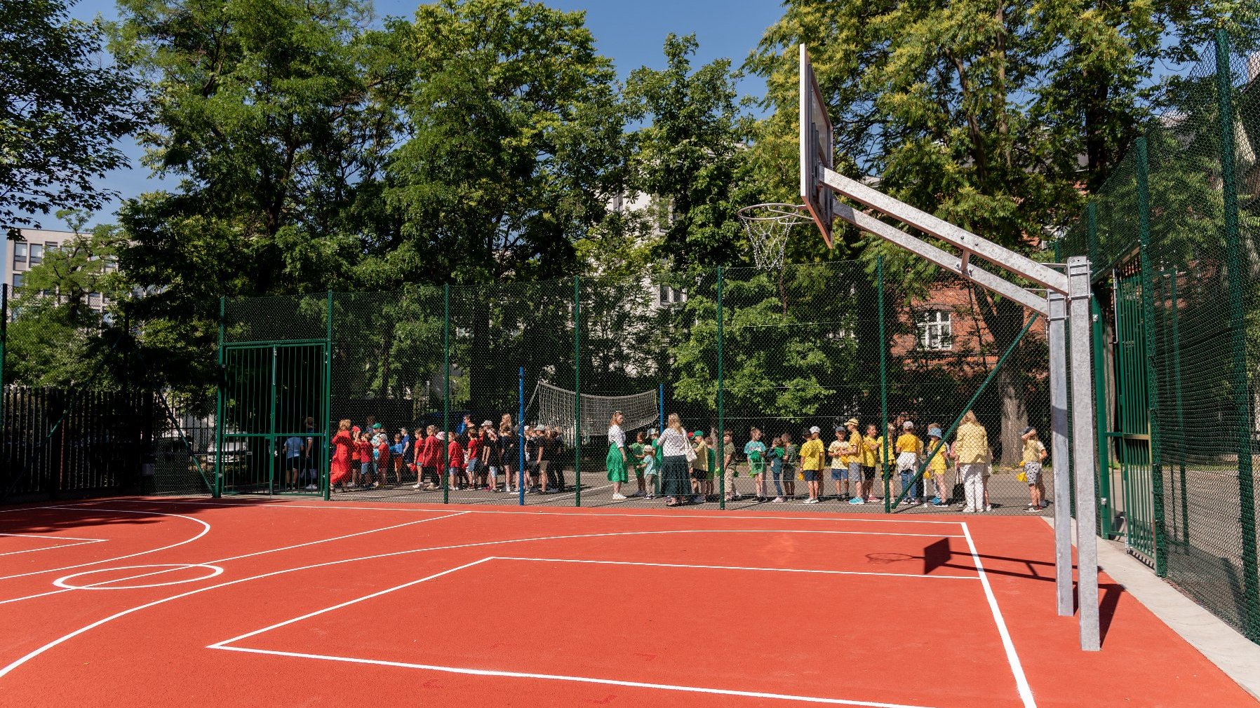 Zdjęcie przedstawia boisko do koszykówki. W tle widać uczniów.