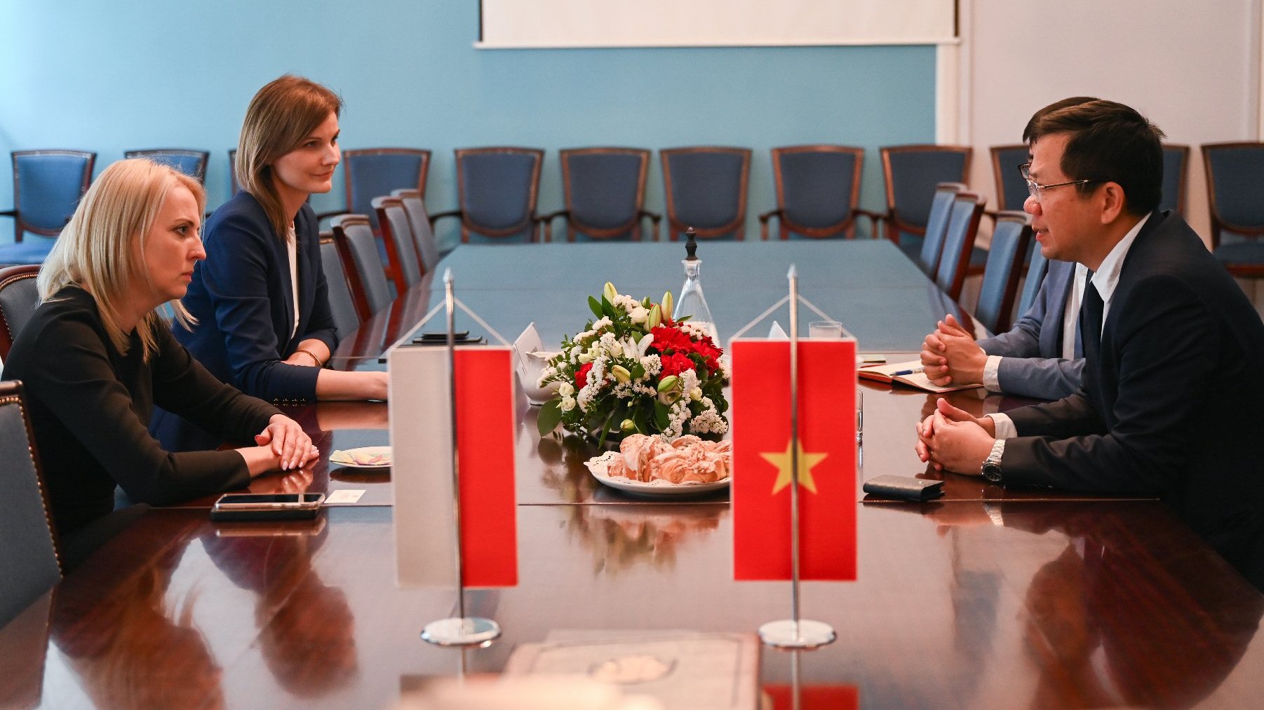 Na zdjęciu cztery osoby przy stole, rozmawiają. Na pierwszym planie polska i wietnamska flaga