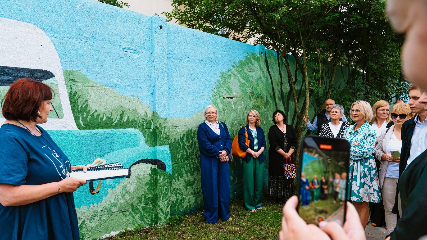 Na zdjęciu kobieta przed muralem coś tłumaczy, słuchają jej inni ludzie