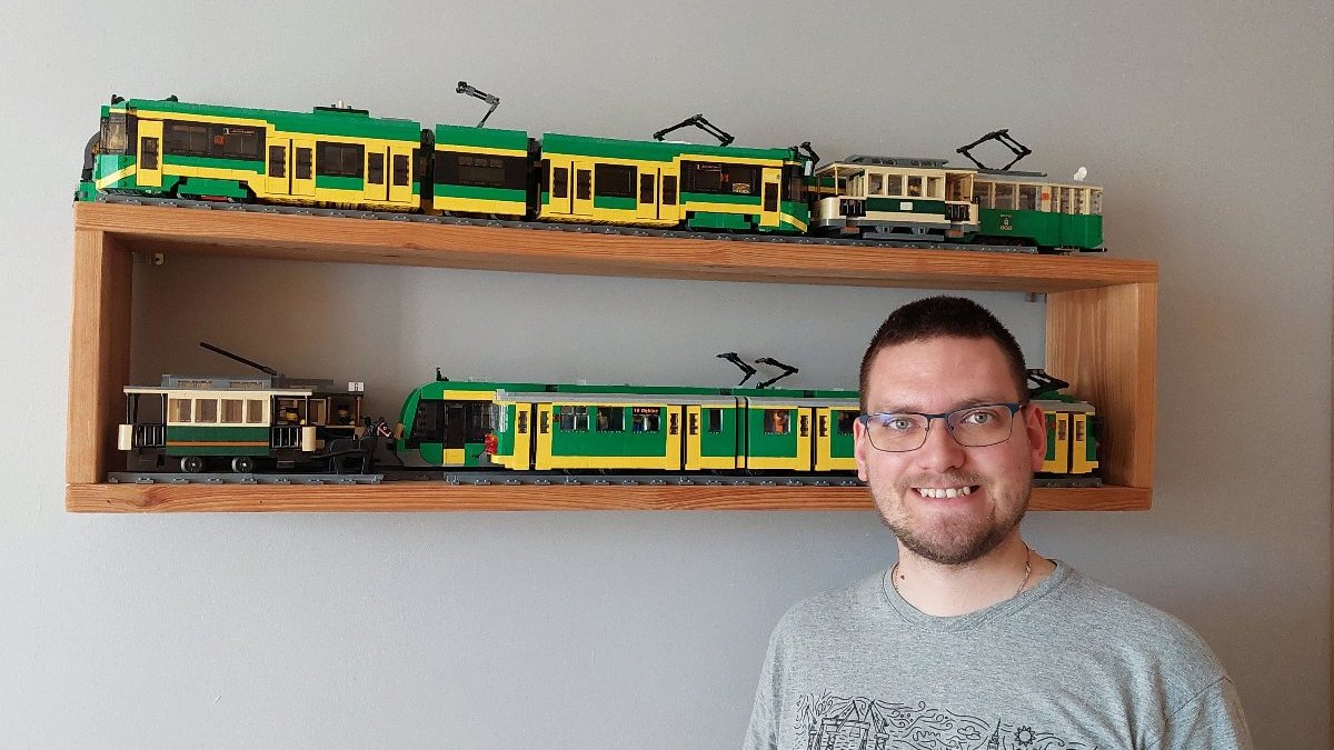 Na zdjęciu mężczyzna, za nim półka z tramwajami z klocków lego