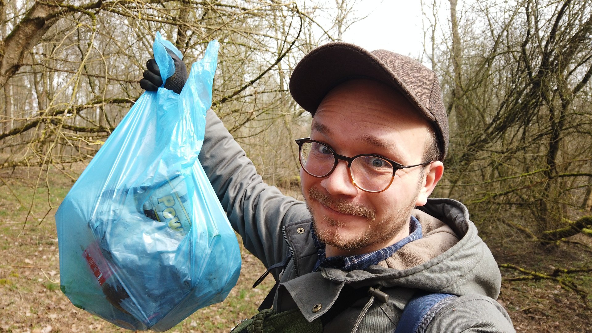 Na zdjęciu mężczyzna w lesie, trzymający w ręku torbę pełną śmieci