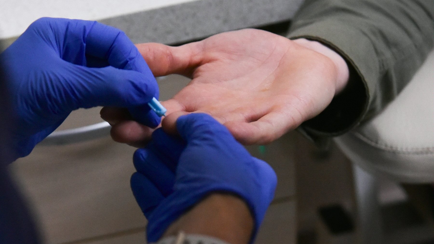 Na zdjęciu ręce w medycznych rękawiczkach pobierają komuś krew z palca