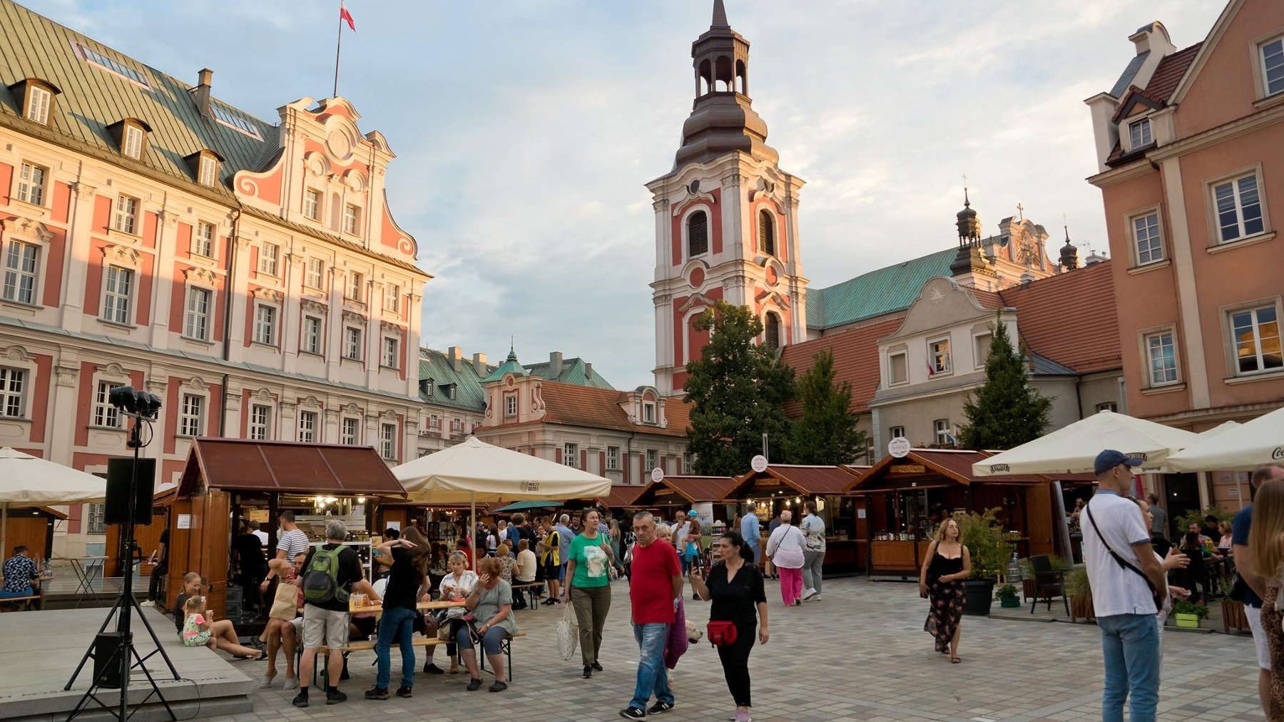 Zdjęcie przedstawia plac Kolegiacki, na kórym stoją stragany i spacerują ludzie.