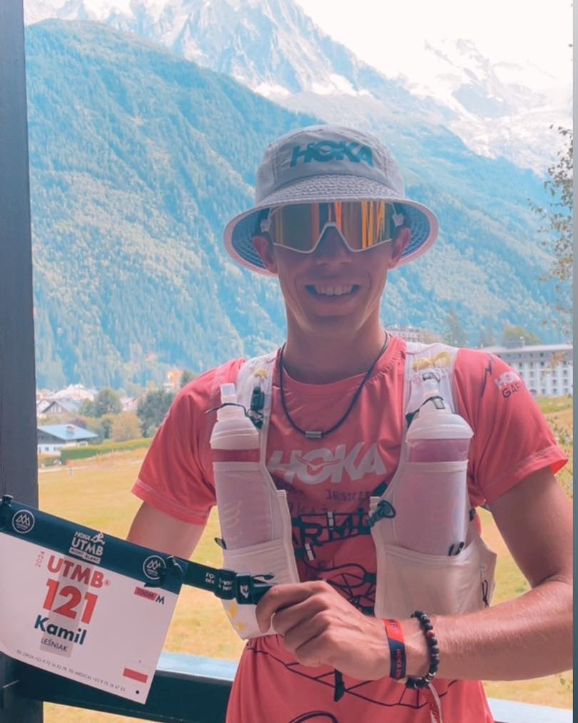 Kamil Leśniak przed rozpoczęciem Ultra-Trail du Mont-Blanc, fot. Facebook Kamil Leśniak - fanpage - mężczyzna trzyma numer startowy na tle Alp - grafika artykułu