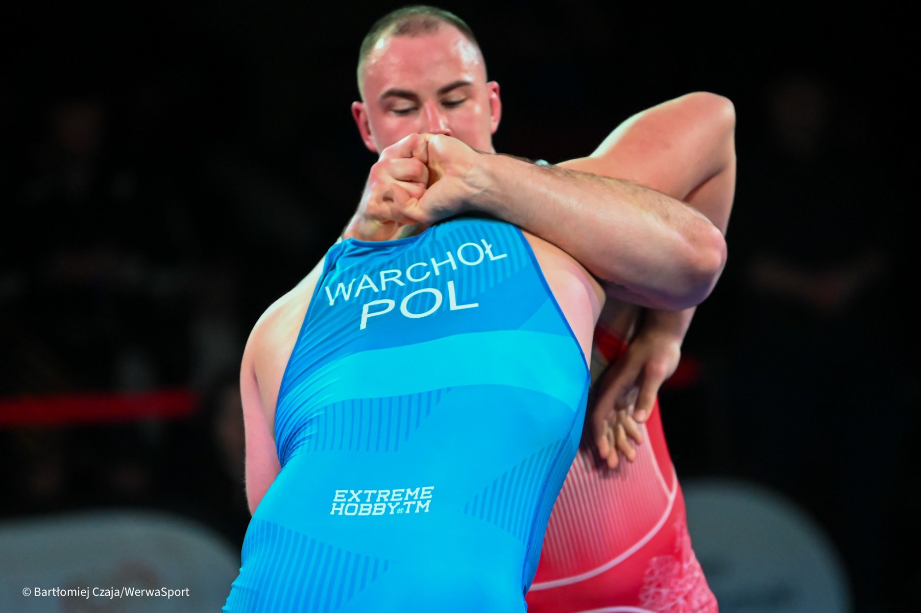 Zawodnicy Sobieskiego Poznań z medalami na MP seniorów, fot. Bartłomiej Czaja - zawodnik w niebieskim stroju jest uchwycony za głowę przez zapaśnika w czerwonym stroju - grafika artykułu