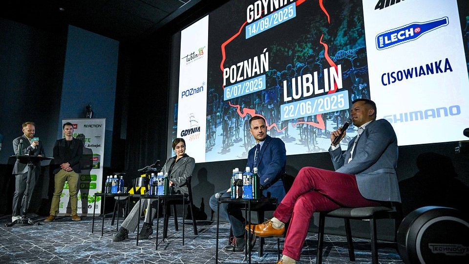 Konferencja prasowa przed cyklem Gran Fondo, fot. Barłomiej Zborowski - na pierwszym planie na krzesłach siedzą goście konferencji, w środku siedzi Zastępca Dyrektora Wydziału Sportu UMP, Dariusz Łapawa. Z lewej strony prowadzący konferencję. W tle lokalizacje, terminy i sponsorzy wyścigów