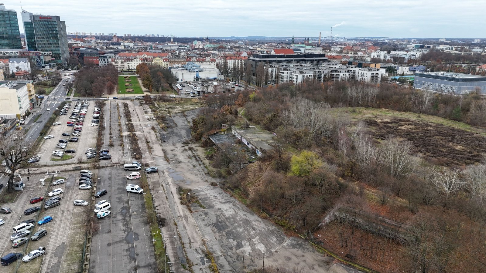 Zdjęcie przedstawia teren miejski z budynkami, drzewami i samochodami. Zdjęcie zrobiono z lotu ptaka.