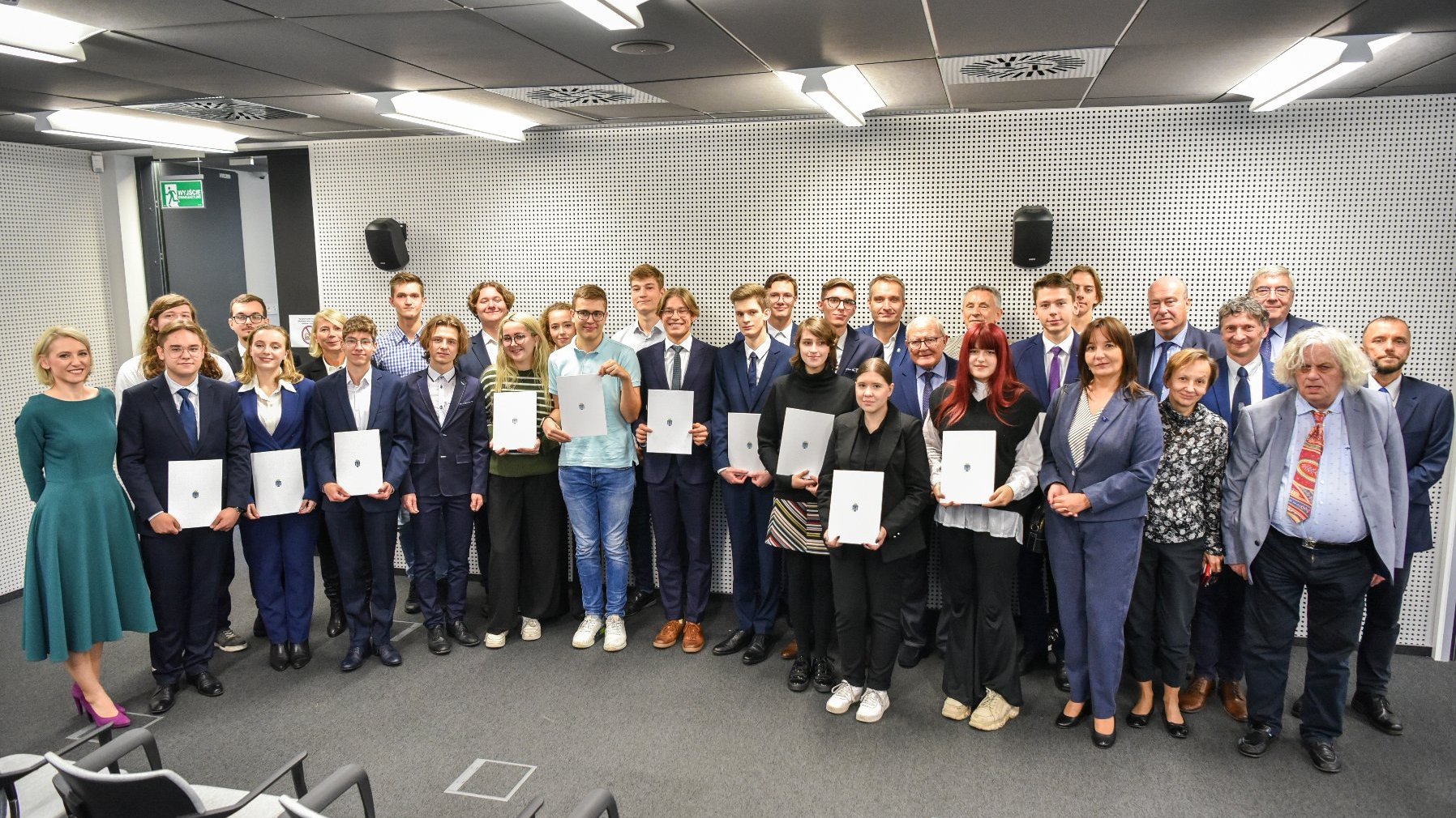 Zdjęcie przedstawia grupę elegancko ubranych osób stojących w sali konferencyjnej