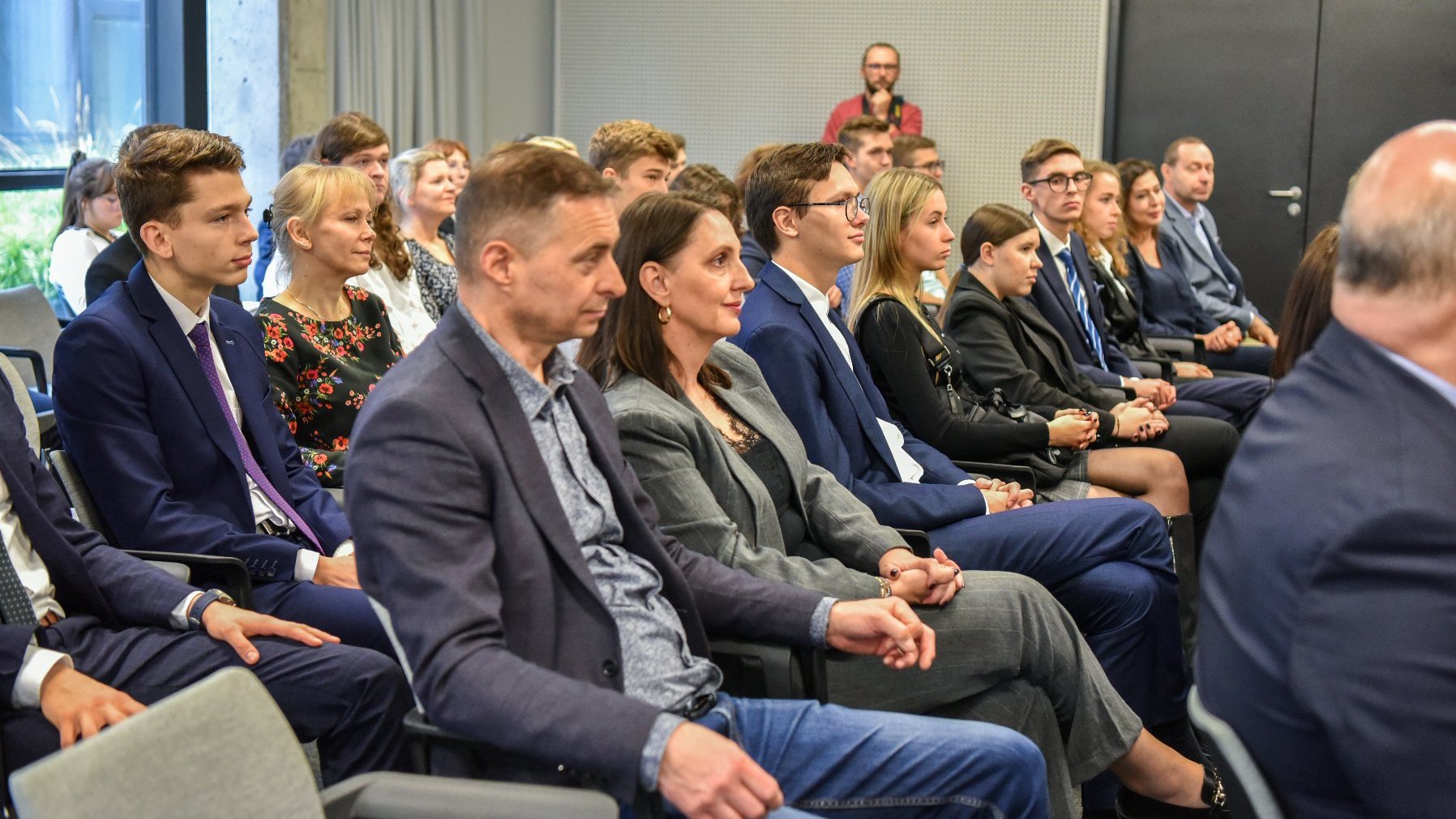 Zdjęcie przedstawia grupę osób siedzących na widowni w sali konferencyjnej