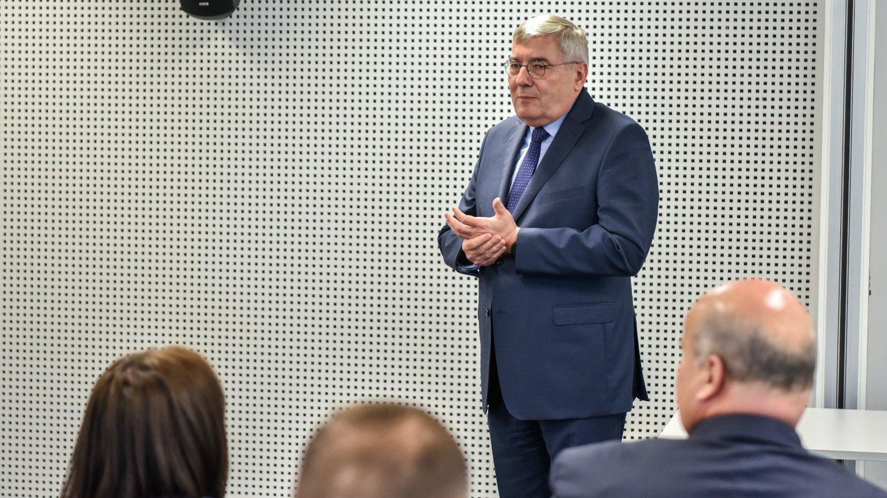 Zdjęcie przedstawia mężczyznę w garniturze przemawiającego w sali konferencyjnej