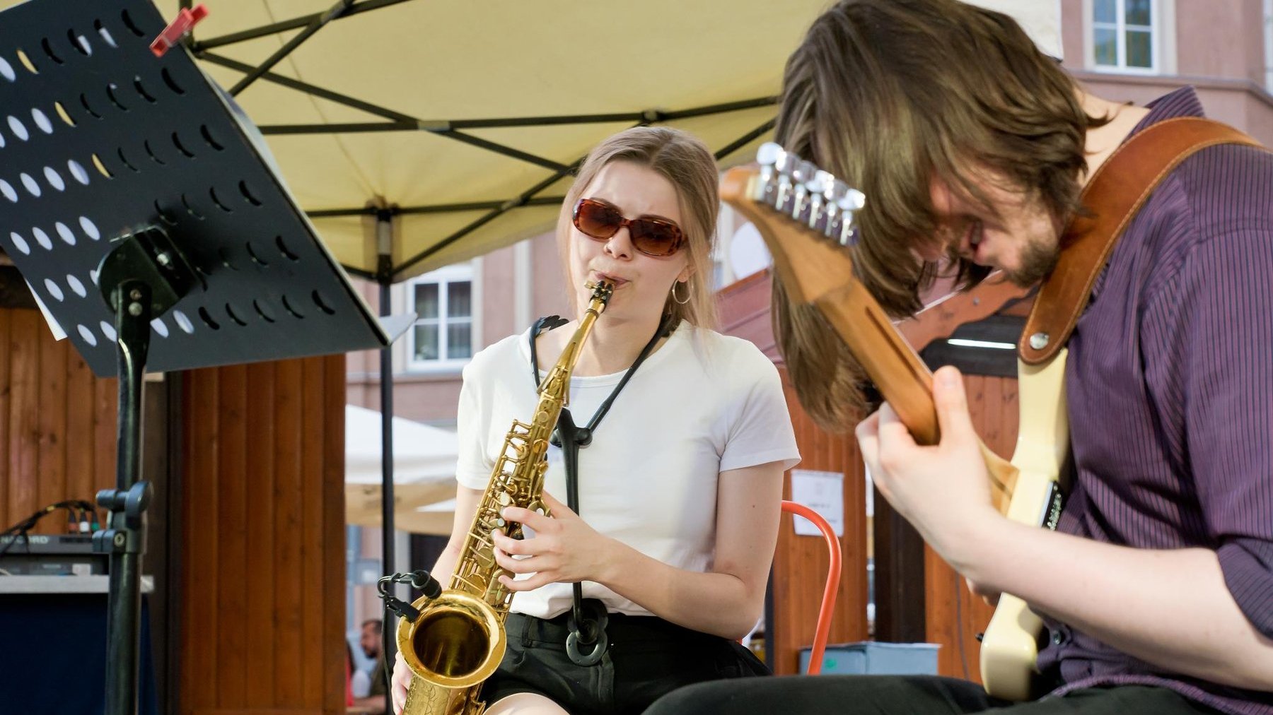 Zdjęcie przedstawia kobietę grającą na saksofonie i mężczyznę grającego na gitarze.