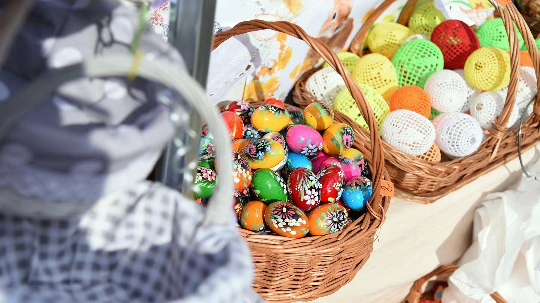 W koszyku kolorowe pisanki, w koszyku obok kolorowe jajka robione na szydełku.