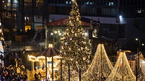 Widok na oświetlony iluminacjami jarmark na MTP. Na pierwszym planie widać udekorowaną wysoką choinkę, za nią karuzela wenecka.