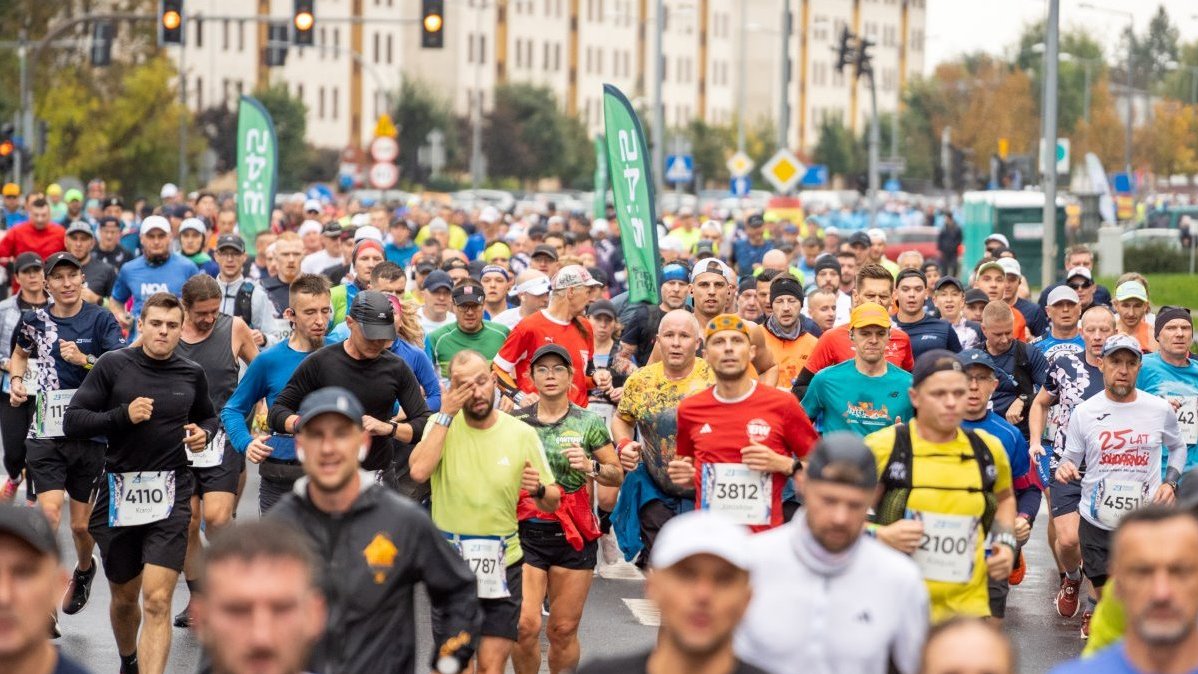 Zdjęcie z trasy zeszłorocznego maratonu. Tłum zawodników biegnie ulicą, w tle widać budynki.