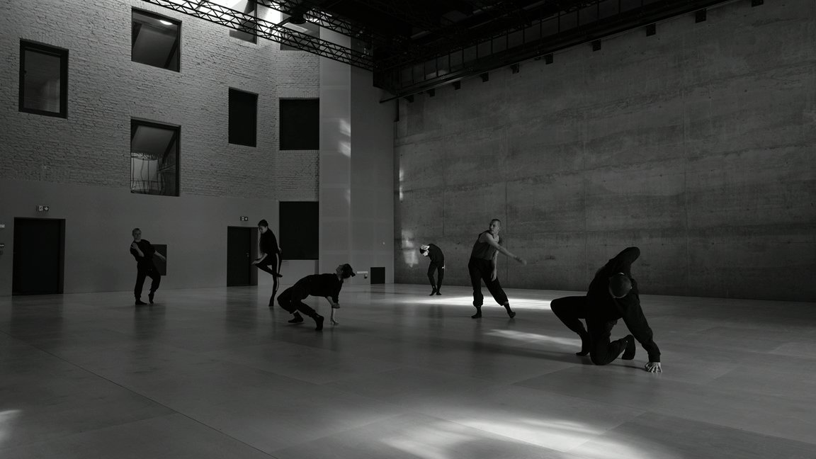 Black and white photo of dancers in various poses in empty, modern space.