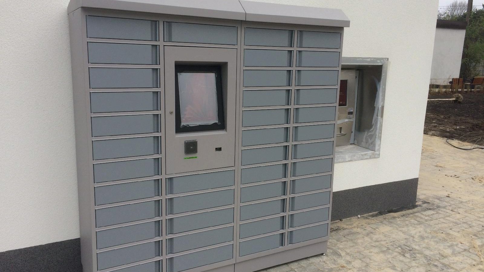 Picture of big, grey book vending machine. There is a white wall in the background. - grafika artykułu