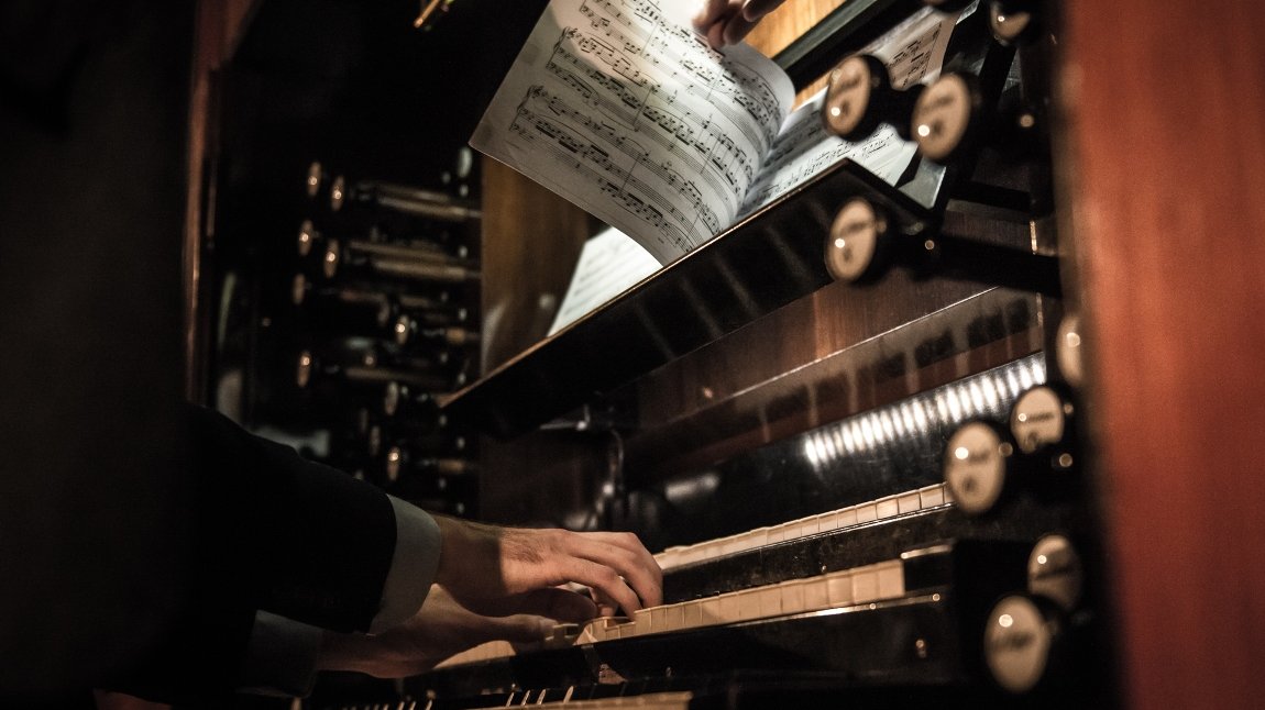 A part of pipe organ. The photo shows a musician's hands on a keyboard and pages with notes