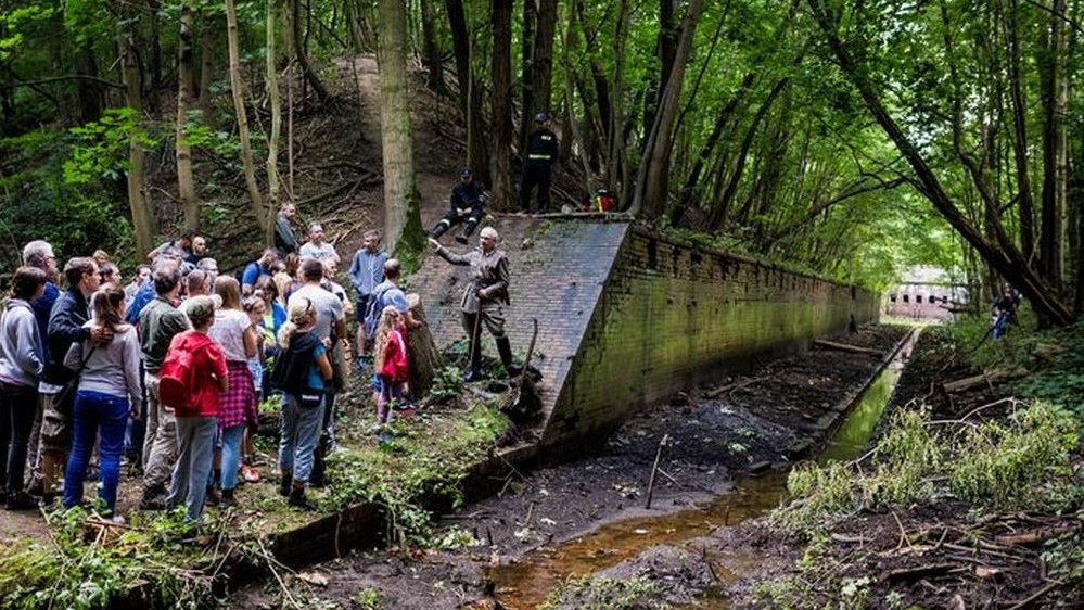 A photo of a group of people standing in a front of the fort situated in a forest.