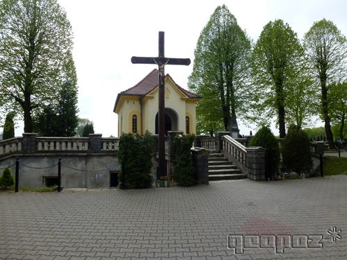 Na środku duży krzyż. Obok schody prowadzą do kaplicy. Po dwóch stronach kaplicy wysokie drzewa.