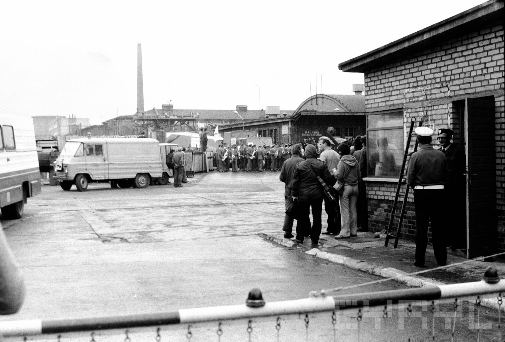 W Zakładach powstał pomnik upamiętniający Poznański Czerwiec / fot. CYRYL Czarno-biała fotografia przedstawia zgromadzonych ludzi na parkinku zakładów HCP. W tle na jednym z samochodów ciężarowych ładowana jest konstrukcja pomnika. W tle budynki zakładu.