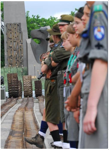 Przed pomnikiem stoją harcerze