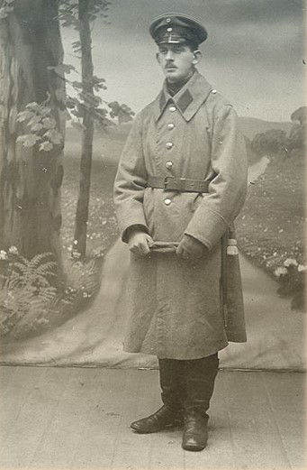 Zdjęcie przedstawia Henryka Śniegockiego, w mundurze, pozującego na tle fototapety ze wzorem polnej drogi.