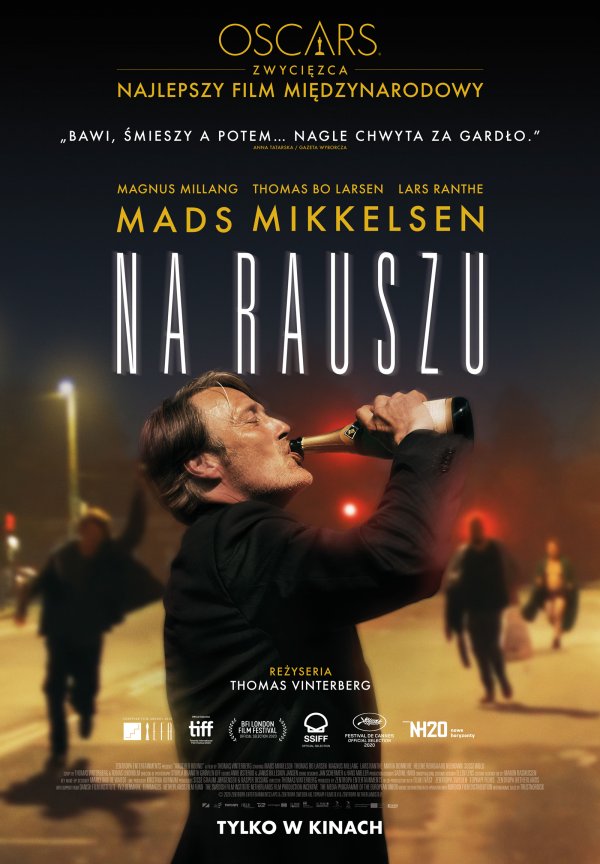 Plakat przedstawia mężczyznę w średnim wieku, w ktorego wciela się aktor Mads Mikkelsen. Mężczyzna stoi bokiem w garniturze i pije szampana prosto z butelki. Za nim niewyraźny, rozmyty obraz ulicy.