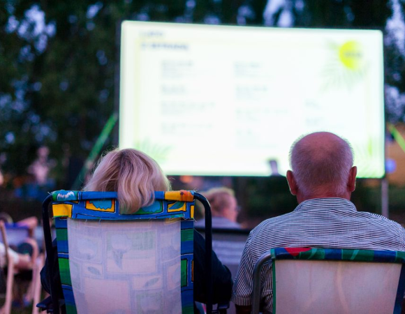 letnie kino plenerowe Na zdjęciu kobieta i mężczyzna siedzący na leżakach tyłem do obiektywu, oglądają film w plenerze