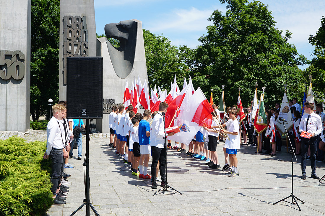 Młodzież z flagami Polski stoi przed pomnikiem