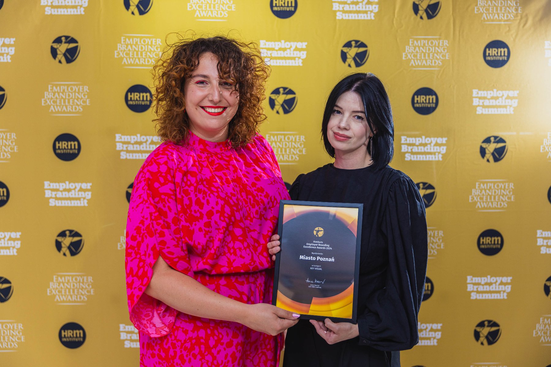 Zdjęcie przedstawia dwie osoby pozujące do zdjęcia. W dłoniach trzymają wyróżnienie w konkursie Employer Branding Excellence Awards 2024. - grafika artykułu