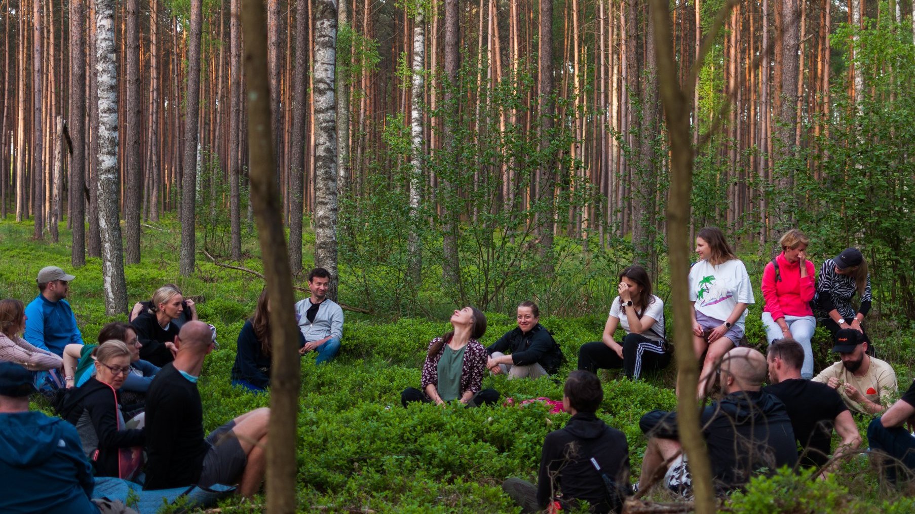 Zdjęcie przedstawia ludzi siedzących w lesie