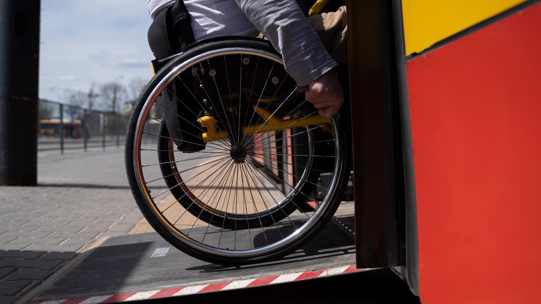 Zdjęcie przedstawia osobę na wózku inwalidzkim wjeżdząjącą do autobusu.