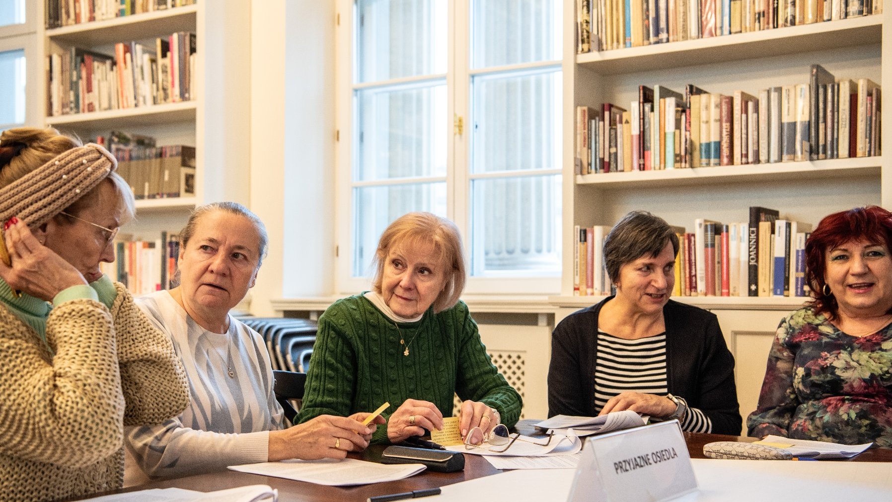 duża jasna sala biblioteki, stolik warsztatowy, przy którym siedzą seniorki. Trwają warsztaty i praca w grupach.