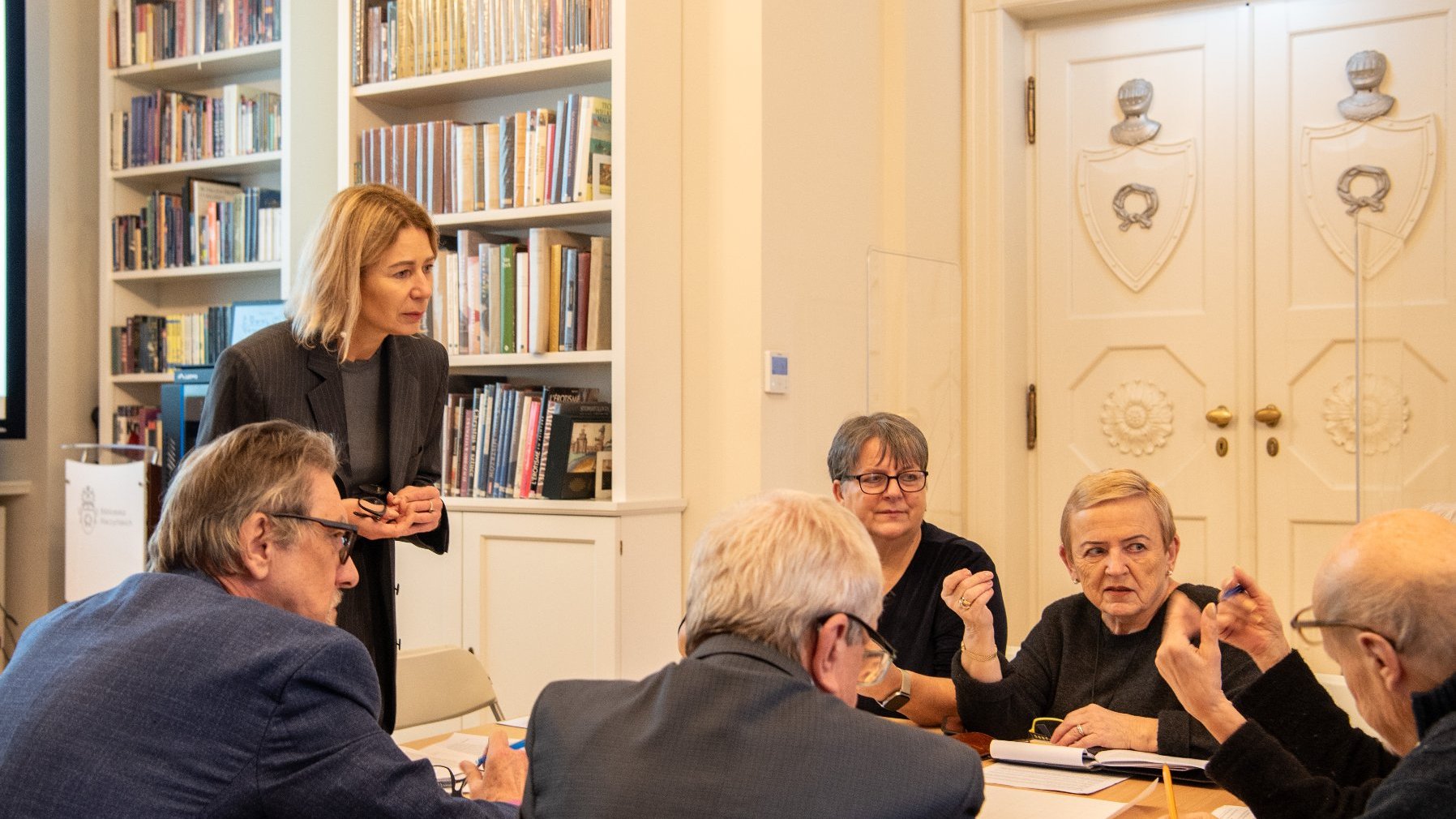 duża jasna sala biblioteki z dużą liczbą stolików, przy których siedzą seniorki i seniorzy. Trwają warsztaty i praca w grupach.