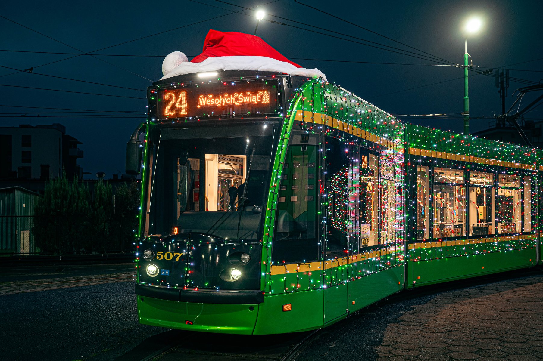 Tramwaj jadący w ciemności oświetlony kolorowymi lampkami i z umieszczoną na górze czapką świętego Mikołaja - grafika artykułu