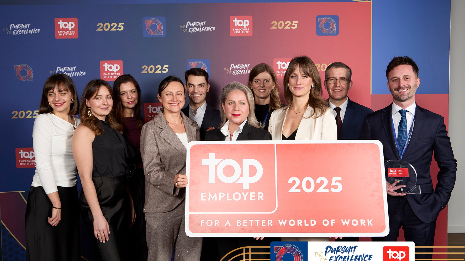 Grupa ludzi ubrana w eleganckie stroje. Pozują z nagrodą-statuetką Top Employer 2025.