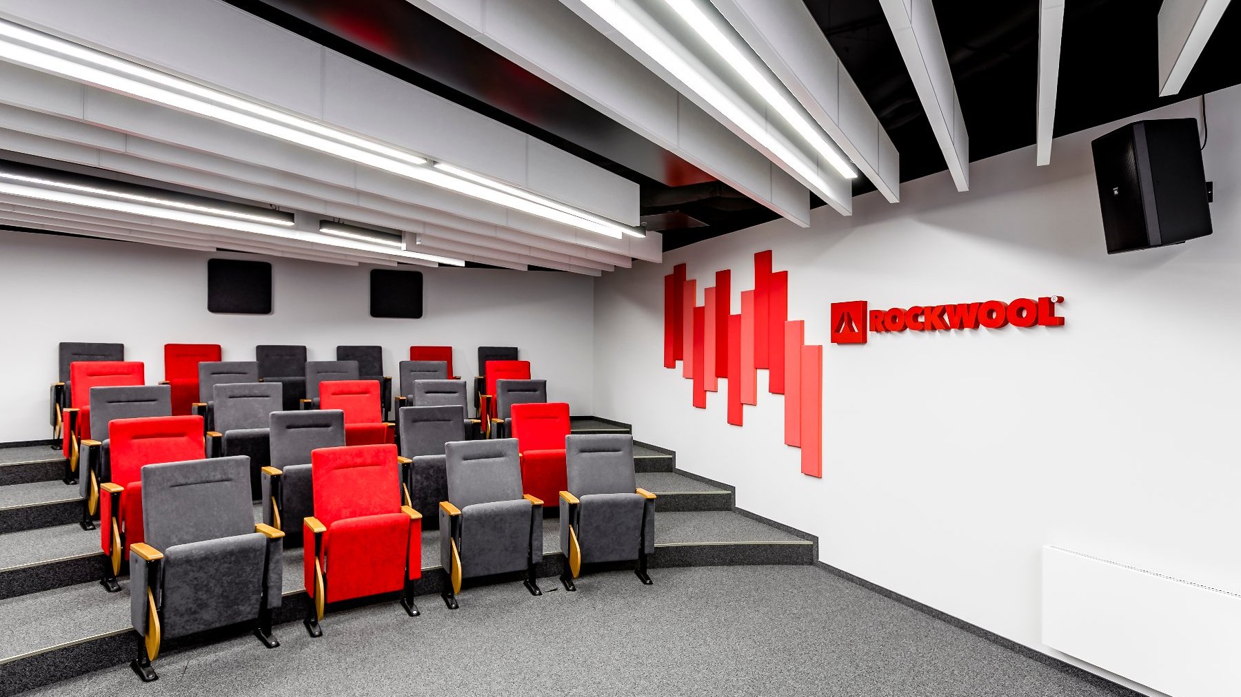 Sala konferencyjna wyłożona szarą wykładziną. Na ścianie logo ROCKWOOL.